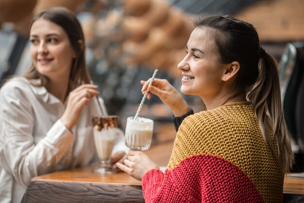 Twee gelukkige vrouwen zitten in een café en drinken milkshakes,