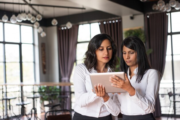 Twee gerichte vrouwelijke collega&#39;s die tabletcomputer in koffie met behulp van.