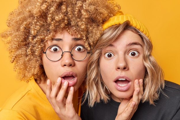 Twee geschokte jonge vrouwen staren naar camera met angstige gezichtsuitdrukkingen adem inhouden kan niet geloven in iets geweldigs gekleed in casual kleding geïsoleerd op gele achtergrond Omg concept