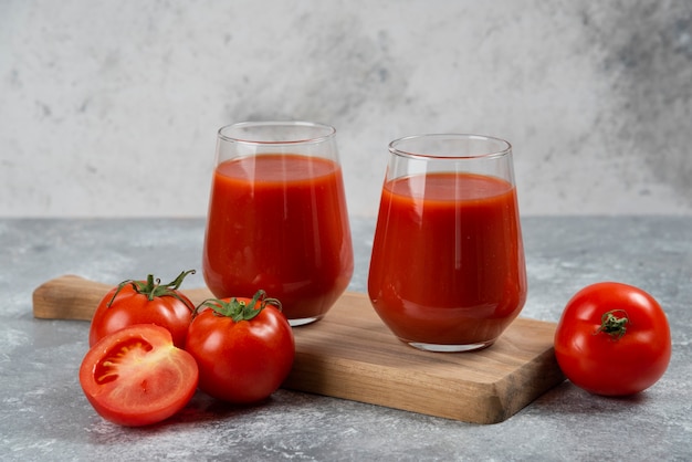 Twee glazen bekers tomatensap op een houten bord.