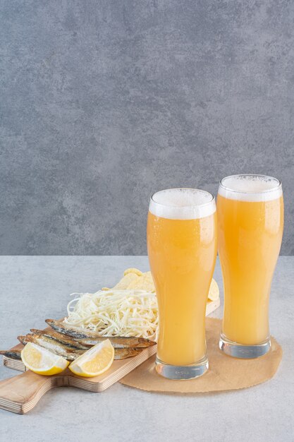 Twee glazen bier met kaas en gesneden citroen op grijs.