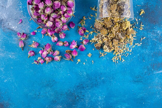 Twee glazen kommen met gedroogde bloemen op blauwe tafel.