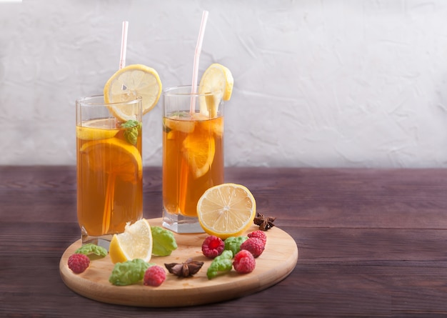 Twee glazen met cocktail buis met kombucha en schijfjes citroen, rietjes en steranijs op een houten tafel.
