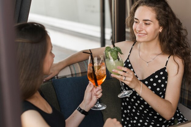 Twee glimlachende jonge vrouwelijke vrienden die cocktailglazen roosteren