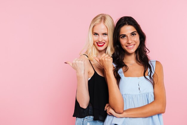 Twee glimlachende vrouwen weg wijzen en kijken naar de camera