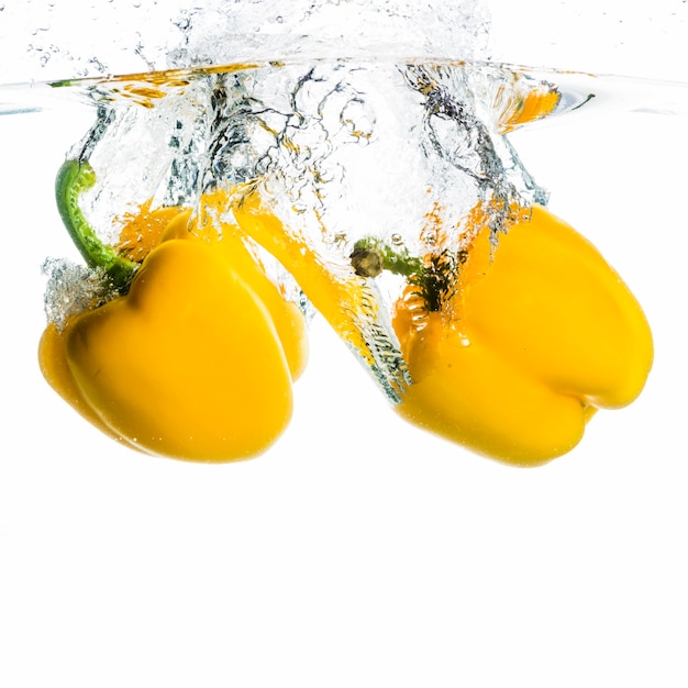 Twee groene paprika die in de waterplons vallen op witte achtergrond