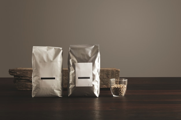 Twee grote hermetische verpakkingen met blanco etiketten bij transparant glas met rauwe bemonsterde koffiebonen