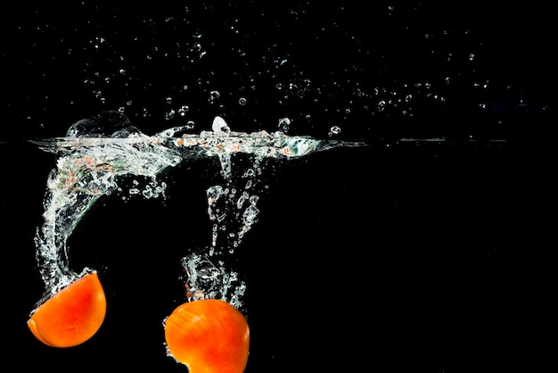 Twee helften tomaten vallen in schoon water met plons