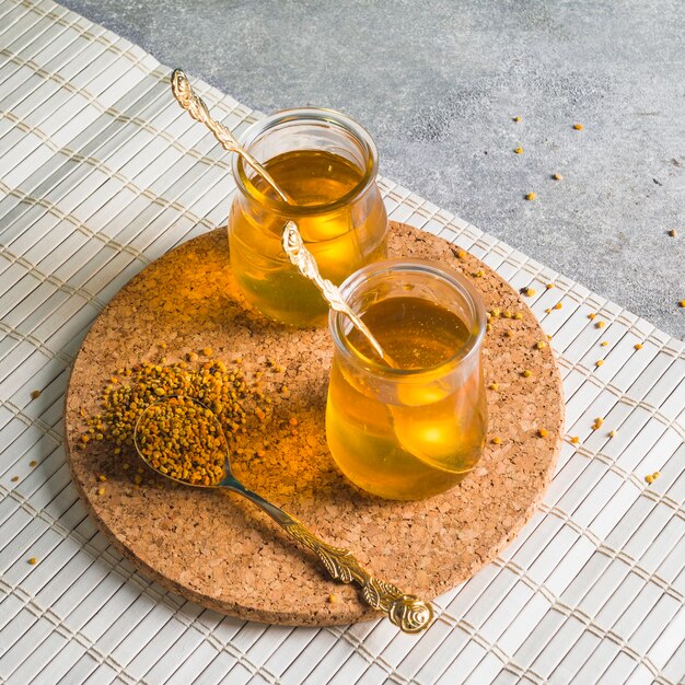 Twee honingpotten met bijenpollen op circulaire cork coaster