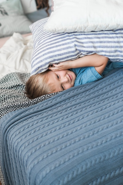 Twee hoofdkussens over de glimlachende kleine jongen die op bed liggen