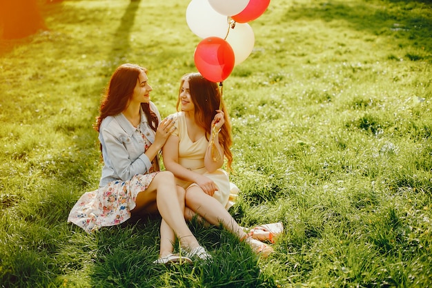 twee jonge en heldere meisjes brengen hun tijd door in het zomerpark met ballonnen