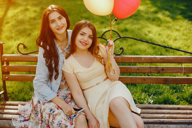 twee jonge en heldere meisjes brengen hun tijd door in het zomerpark met ballonnen