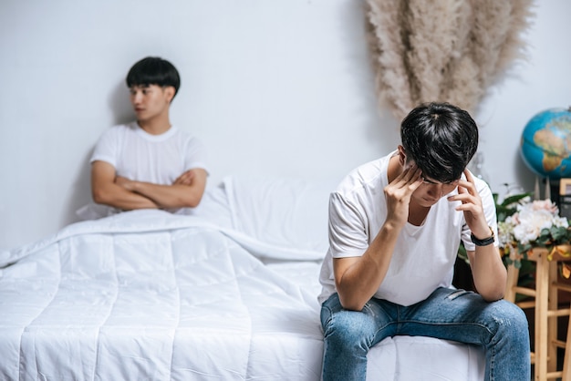 Twee jonge mannen lagen boos op het bed en de andere zat aan de rand van het bed en was gestrest.