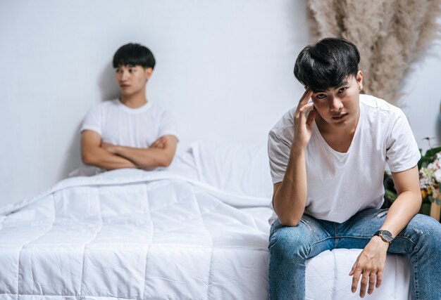 Twee jonge mannen lagen boos op het bed en de andere zat aan de rand van het bed en was gestrest.