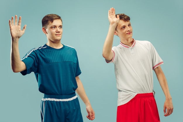 Gratis foto twee jonge mannen staan en begroeten in sportkleding geïsoleerd op blauw