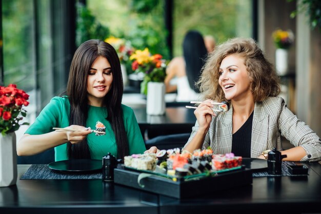 Twee jonge meisjes zitten in een restaurant op het zomerterras en brengen grappige tijd door met bord philadelphia.