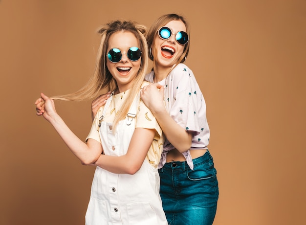 Twee jonge mooie glimlachende blonde hipstermeisjes in kleren van de trendy de zomer kleurrijke T-shirt.