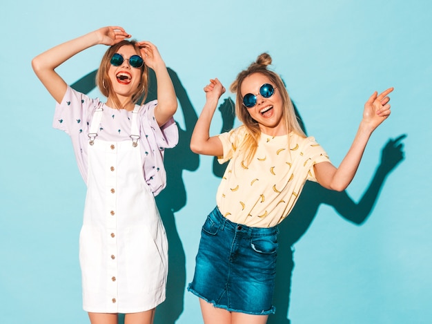 Twee jonge mooie glimlachende blonde hipstermeisjes in kleren van de trendy de zomer kleurrijke t-shirt.