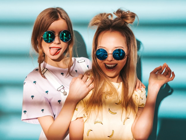 Twee jonge mooie glimlachende blonde hipstermeisjes in kleren van de trendy de zomer kleurrijke t-shirt.