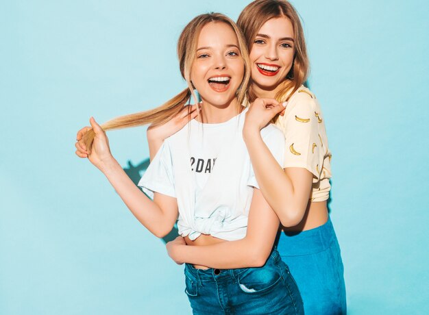 Twee jonge mooie glimlachende blonde hipstermeisjes in kleren van de trendy de zomer kleurrijke T-shirt.