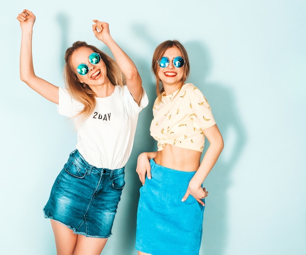Twee jonge mooie glimlachende blonde hipstermeisjes in kleren van de trendy de zomer kleurrijke T-shirt.