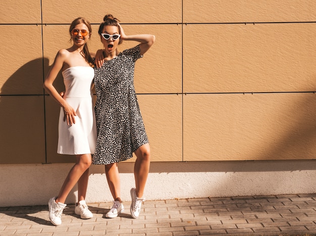 Twee jonge mooie glimlachende hipster meisjes in trendy zomer jurken.