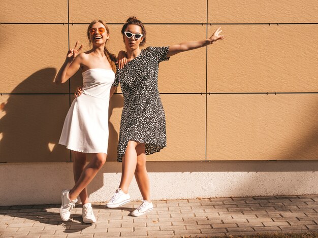 Twee jonge mooie glimlachende hipster meisjes in trendy zomer jurken.
