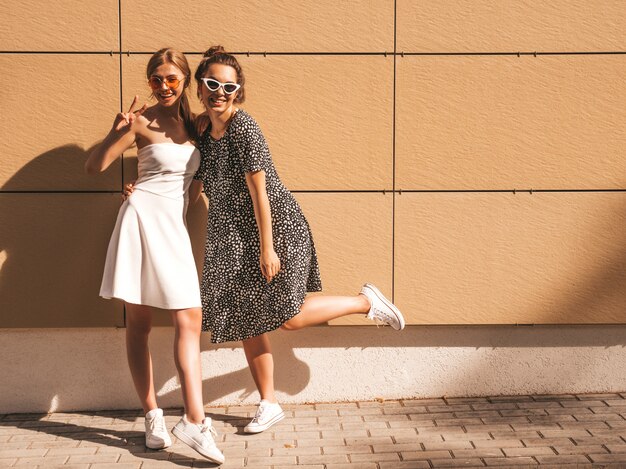 Twee jonge mooie glimlachende hipster meisjes in trendy zomer jurken.