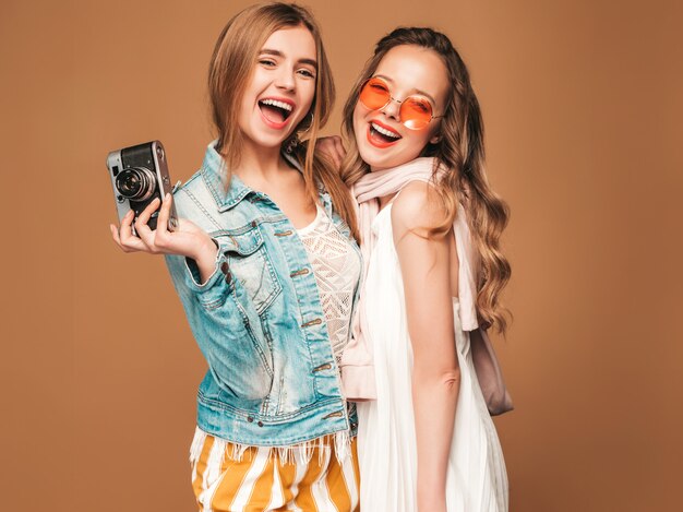 Twee jonge mooie glimlachende meisjes in trendy zomer casual kleding en zonnebril. Sexy zorgeloze vrouwen poseren. Foto's maken met een retro camera