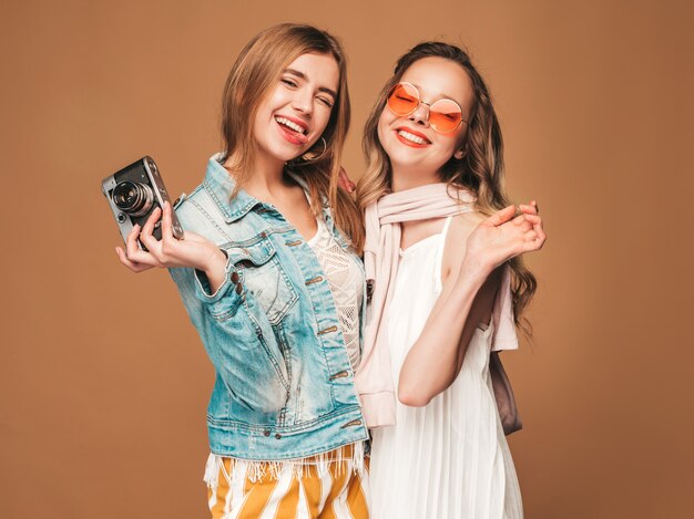 Twee jonge mooie glimlachende meisjes in trendy zomer casual kleding en zonnebril. Sexy zorgeloze vrouwen poseren. Foto's maken met een retro camera
