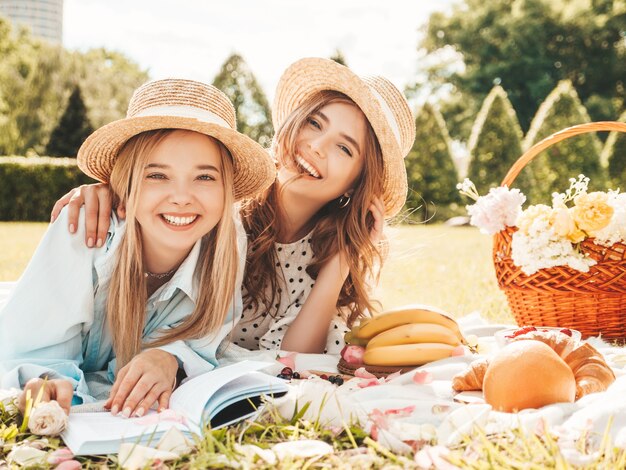 Twee jonge mooie glimlachende vrouw in trendy zomerjurk en hoeden. Zorgeloze vrouwen die buiten picknicken.