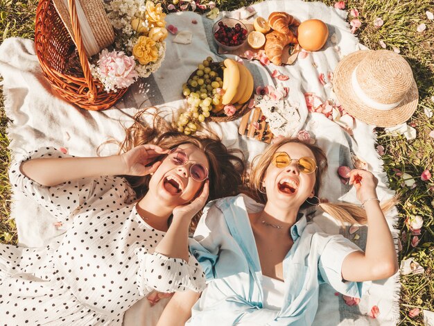 Twee jonge mooie glimlachende vrouw in trendy zomerjurk en hoeden. Zorgeloze vrouwen die buiten picknicken.