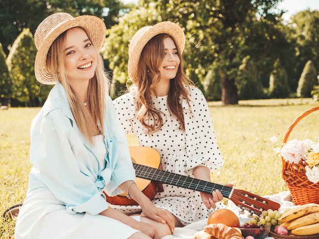 Twee jonge mooie hipster vrouw in trendy zomerjurk en hoeden. Zorgeloze vrouwen die buiten picknicken.
