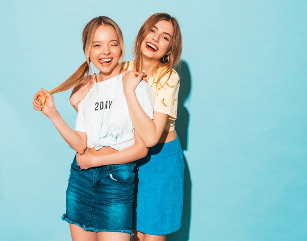 Twee jonge mooie lachende blonde hipster meisjes in trendy zomer jeans rokken kleding.