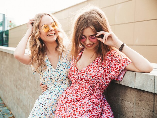 Twee jonge mooie lachende hipster meisjes in trendy zomer sundress. Sexy zorgeloze vrouwen die zich voordeed op de straat achtergrond in zonnebril. Positieve modellen die plezier hebben en gek worden