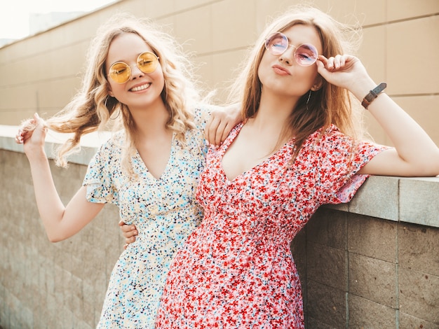 Twee jonge mooie lachende hipster meisjes in trendy zomer sundress. Sexy zorgeloze vrouwen die zich voordeed op de straat achtergrond in zonnebril. Positieve modellen die plezier hebben en knuffelen