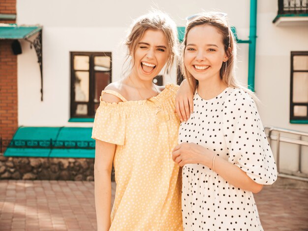 Twee jonge mooie lachende hipster meisjes in trendy zomer sundress. Sexy zorgeloze vrouwen die zich voordeed op de straat achtergrond in zonnebril. Positieve modellen die plezier hebben en knuffelen