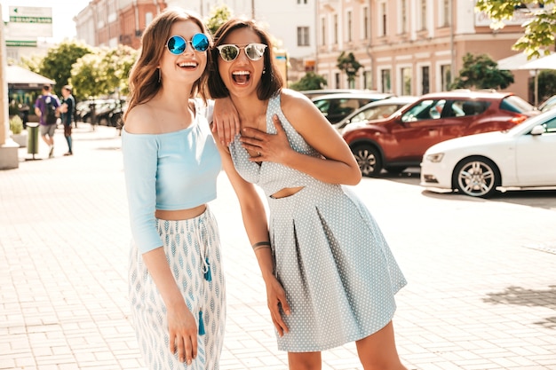 Twee jonge mooie lachende hipster meisjes in trendy zomerkleding. sexy zorgeloze vrouwen die zich voordeed op straat achtergrond in zonnebril. positieve modellen die plezier hebben en knuffelen
