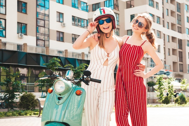 Twee jonge mooie lachende hipster vrouw in trendy overallsSexy zorgeloze vrouwen retro motor rijden op de straat achtergrond Positieve modellen plezier rijden klassieke Italiaanse scooter in brillen