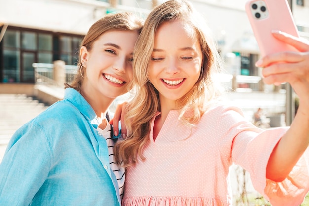 Twee jonge mooie lachende hipster vrouw in trendy zomer kleding en dresssexy zorgeloze vrouwen poseren in de straatpositieve pure modellen plezier haar vriend kussen in de wang selfie nemen