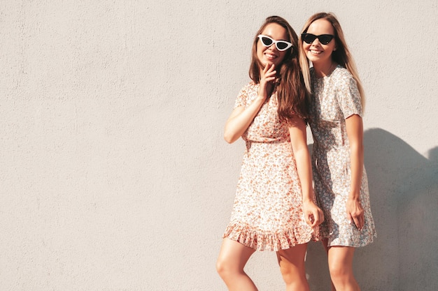 Twee jonge mooie lachende hipster vrouw in trendy zomerjurken zorgeloze vrouwen poseren op de straat achtergrond in de buurt van witte muur positieve pure modellen plezier bij zonsondergang knuffelen