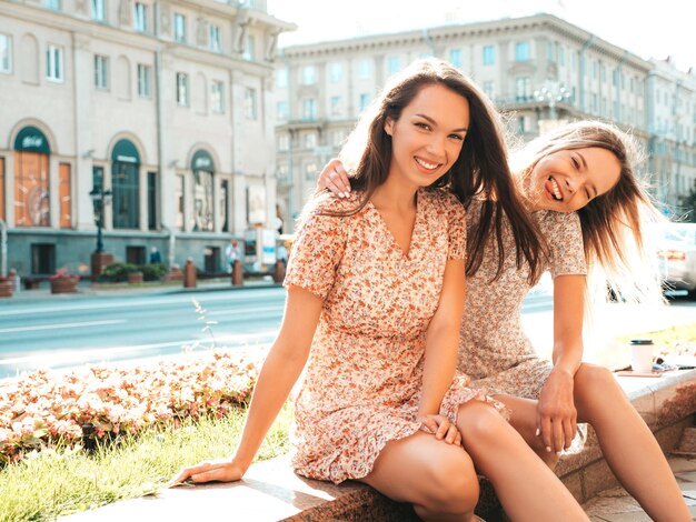 Twee jonge mooie lachende hipster vrouw in trendy zomerjurkenSexy zorgeloze vrouwen poseren in de straat Positieve pure modellen plezier bij zonsondergang knuffelen en gek worden
