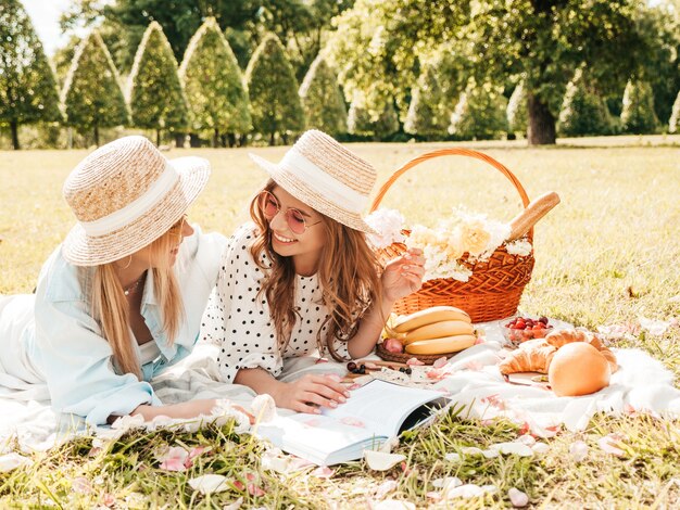 Twee jonge mooie lachende hipster vrouw in zomer sundress en hoeden. Zorgeloze vrouwen picknick buiten maken.