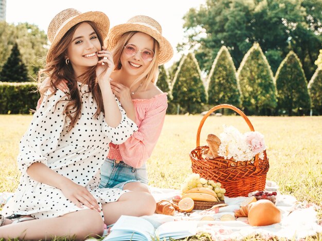 Twee jonge mooie lachende hipster vrouw in zomer sundress en hoeden. Zorgeloze vrouwen picknick buiten maken.