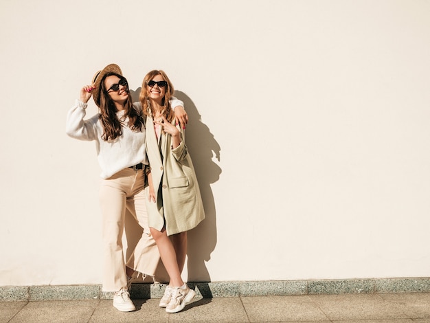 Twee jonge mooie lachende hipster-vrouwen in trendy witte trui en jas