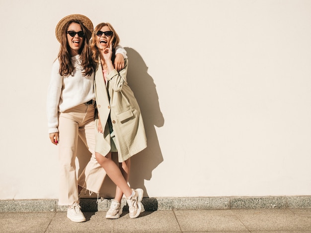 Twee jonge mooie lachende hipster-vrouwen in trendy witte trui en jas