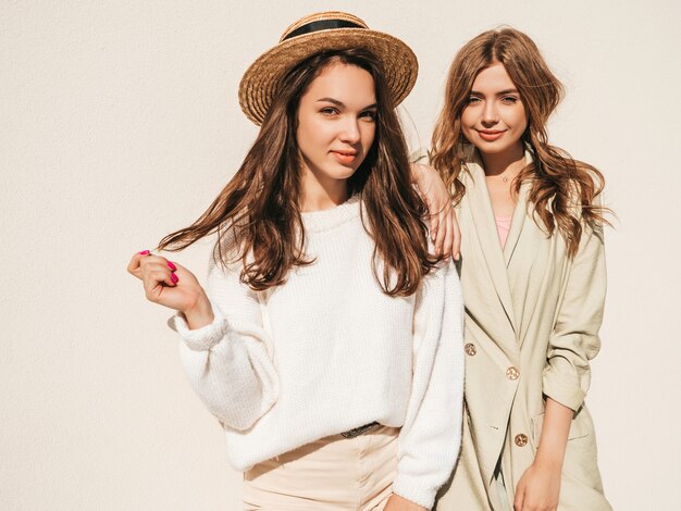 Twee jonge mooie lachende hipster-vrouwen in trendy witte trui en jas