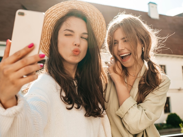 Twee jonge mooie lachende hipster-vrouwen in trendy witte trui en jas