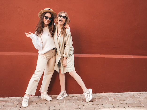 Twee jonge mooie lachende hipster-vrouwen in trendy witte trui en jas