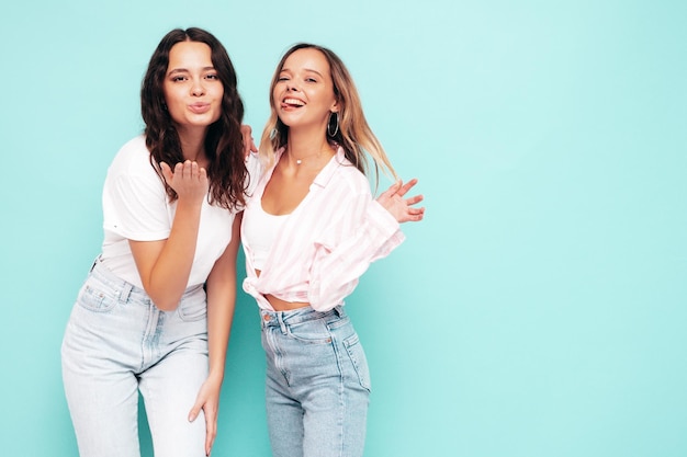 Twee jonge mooie lachende internationale hipster vrouw in trendy zomerkleren Sexy zorgeloze vrouwen poseren in de buurt van blauwe muur in studio Positieve modellen plezier Concept van vriendschap